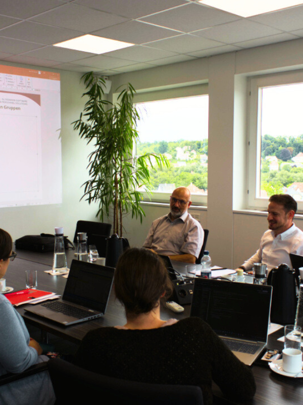 Workshop zur internen Auditierung im Qualitätsmanagementsystem: Führungskräfte und Mitarbeitende diskutieren Schnittstellen und Prozessqualität im Besprechungsraum mit Präsentation.