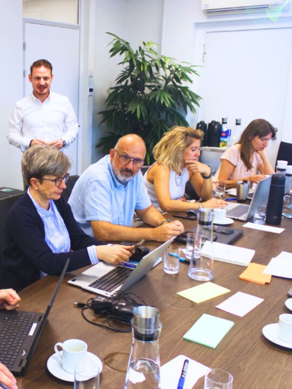 Team-Workshop im Rahmen eines internen Qualitätsmanagementsystems: Führungskraft moderiert, Mitarbeitende arbeiten an Laptops und optimieren interne Kunden-Lieferanten-Beziehungen.