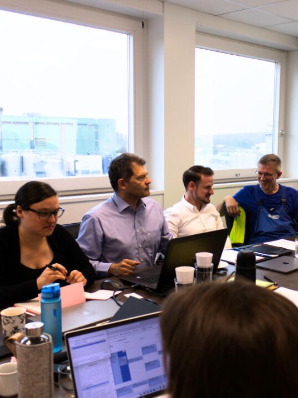 Team im Besprechungsraum diskutiert im Rahmen des internen Qualitätsmanagementsystems die Umsetzung von Maßnahmen zur Optimierung interner Prozesse und Schnittstellen.